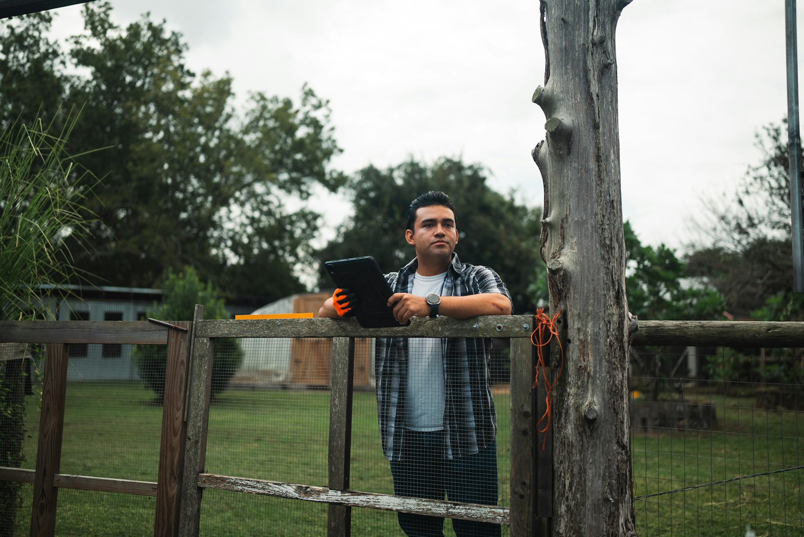 Farmer holding a tablet by a wooden fence